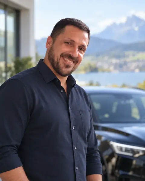 نور، مالك Noor Car Rental، مبتسمًا أمام سيارة إيجار داكنة، وخلفه بحيرة وجبال
